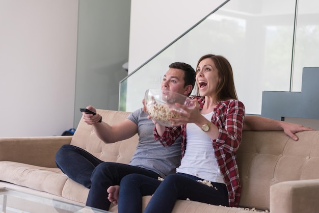 junges hübsches paar, das seine freizeit beim fernsehen mit popcorn in seiner luxusvilla genießt