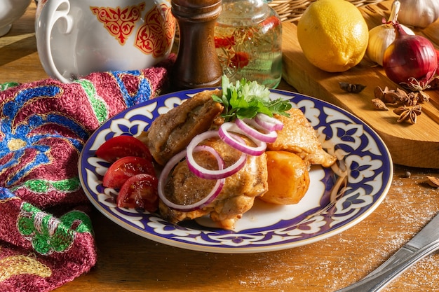 Junges Huhn in Gewürzen, goldbraun gebacken mit Kartoffeln, roten Zwiebeln und Tomaten in einem Teller mit traditionellen usbekischen Ornamenten