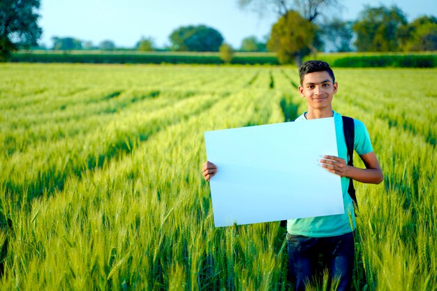 Junges indisches Kind mit leerem Plakat am indischen Weizenfeld