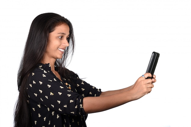 Junges indisches Mädchen, das ein Mobiltelefon oder Smartphone lokalisiert auf einem weißen Raum verwendet