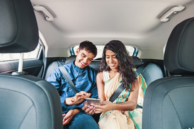 Junges indisches Paar mit Handy auf dem Rücksitz eines Autos