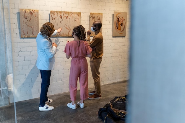 Junges interkulturelles Paar in Masken, das einem reifen Künstler zuhört