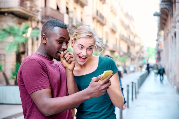 junges interracial paar überrascht mit dem mobilen bildschirm