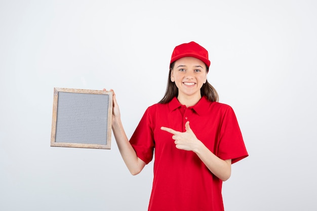 junges jugendlich Mädchen in der roten Uniform stehend und auf Rahmen zeigend