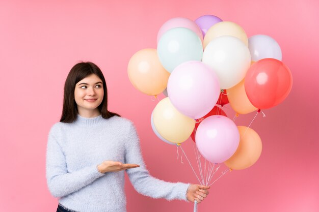 Junges Jugendlichmädchen, das viele Ballone über Erweiterungshänden der rosa Wand zur Seite hält, damit die Einladung kommt