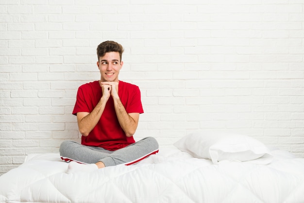 Junges Jugendlichstudenten-Mannbett hält Hände unter Kinn, schaut glücklich beiseite.