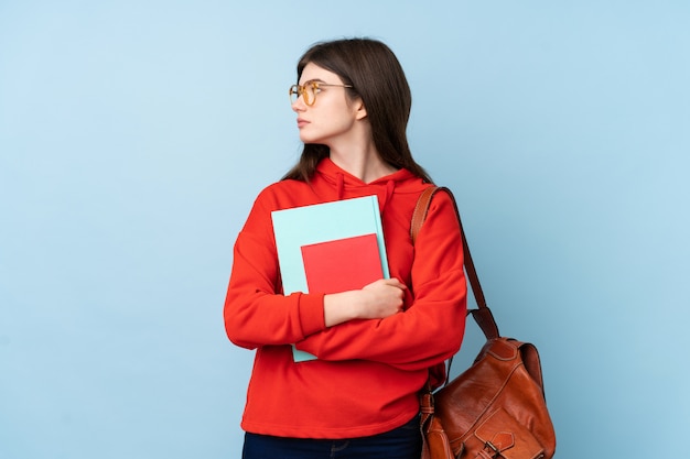 Junges Jugendlichstudentenmädchen, das einen Salat über der blauen Wand schaut Seite hält