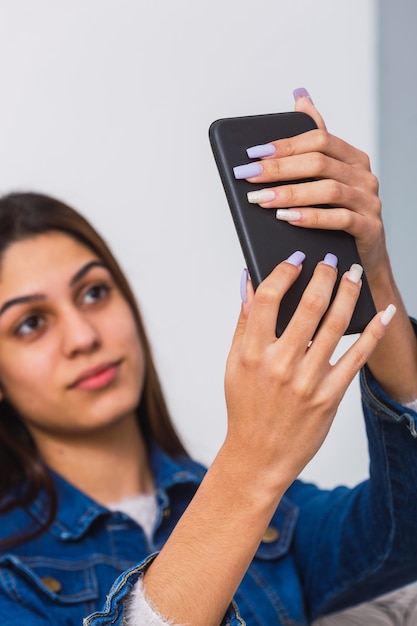 Junges junges Mädchen, das ein sefie nimmt - Porträt einer jungen Frau mit langen Fingernägeln, die ein smathphone halten, während sie ein selfie nehmen.