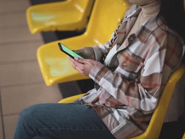 Junges kaukasisches Mädchen hält ein Smartphone mit einem grünen Bildschirm in ihren Händen