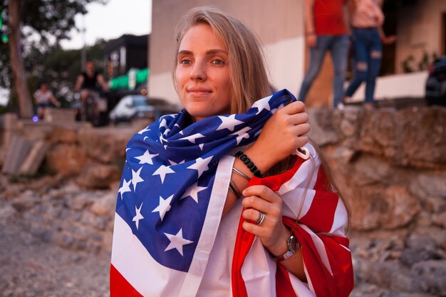 Foto junges kaukasisches mädchen hält eine amerikanische flagge in den händen mit dem meer im hintergrund bei sonnenuntergang