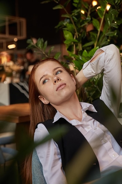 Junges kaukasisches Mädchen mit langen Haaren, das mit dem Kinn nach oben auf einem Stuhl im Café liegt