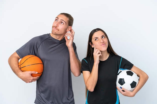 Junges kaukasisches Paar, das Basketball und Fußball spielt, isoliert auf weißem Hintergrund, denkt an eine Idee, während es sich den Kopf kratzt