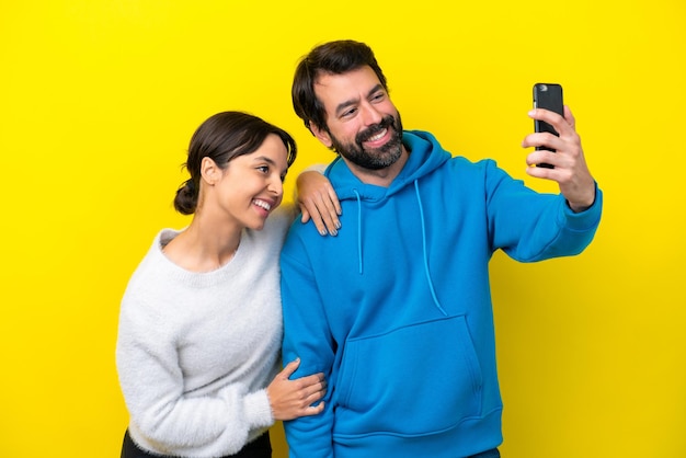 Junges kaukasisches Paar isoliert auf gelbem Hintergrund, das ein Selfie mit dem Handy macht