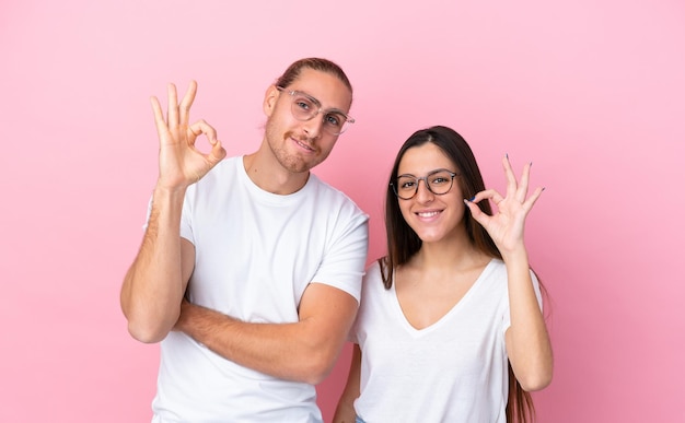 Junges kaukasisches Paar isoliert auf rosa Hintergrund mit Brille und OK-Zeichen