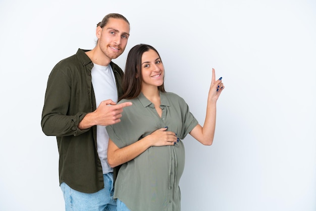 Junges kaukasisches Paar isoliert auf weißem Hintergrund schwanger und zeigt auf die Seite