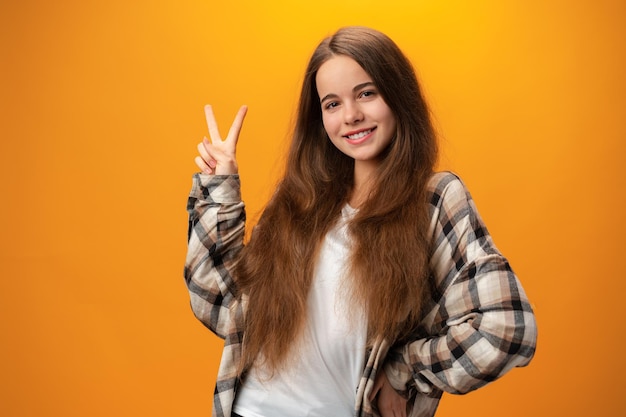 Junges kaukasisches Teenagermädchen, das ein Friedenssymbol vor gelbem Hintergrund zeigt