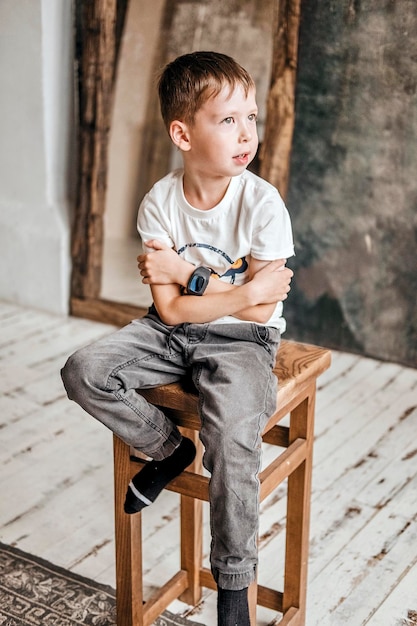 Junges kleines kaukasisches Kind mit grünen Augen, das ein weißes T-Shirt trägt, das eine Armbanduhr hält, die mit einem entspannten Ausdruck wegschaut