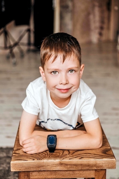 Junges kleines kaukasisches Kind mit grünen Augen in einem weißen T-Shirt mit einer Armbanduhr, die mit einem entspannten Ausdruck in die Kamera blickt