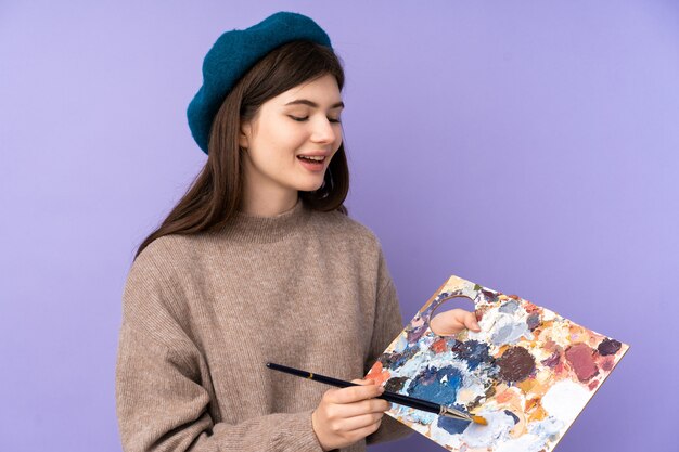 Junges Künstlermädchen, das eine Palette über lila Wand hält