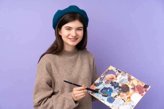 Junges Künstlermädchen, das eine Palette über purpurroter Wand hält