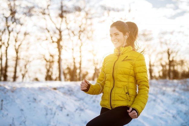 Junges lächelndes und konzentriertes sportliches aktives mädchen mit einem pferdeschwanz, der im winter die schneebedeckte natur am morgen wärmt.