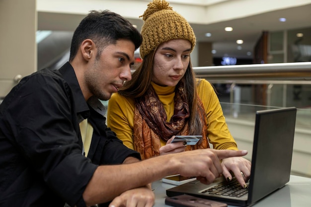 Junges lateinamerikanisches Paar hält eine Kreditkarte in der Hand und benutzt einen Laptop und ein Handy