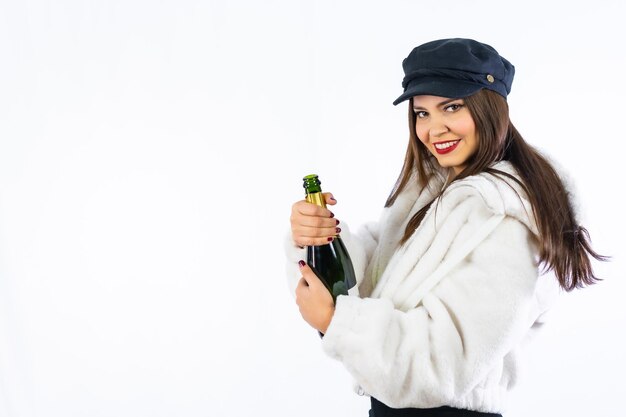 Junges lateinisches Mädchen mit schwarzem Hut, das Silvester auf einem weißen Hintergrund feiert. Öffnen einer Flasche Champagner sehr lächelnd