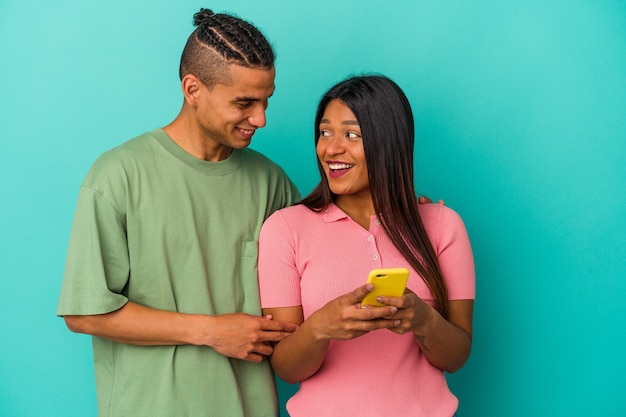 Junges lateinisches Paar mit einem Handy auf blauem Hintergrund isoliert