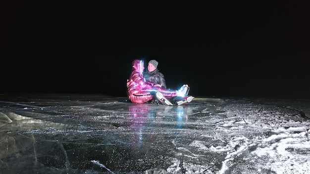 Junges Liebespaar Schlittschuhlaufen auf der Eisbahn in der Nacht Mann und Frau küssen Umarmung viel Spaß Schlittschuhlaufen lernen Liebesspiel auf Eis Eis beleuchtete Hintergrundbeleuchtung unten