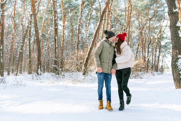 Junges Liebespaar steht im Winterwald, sieht sich an und reibt sich die Nase, hält sich an den Händen Menschen im Freien Vertikaler Rahmen