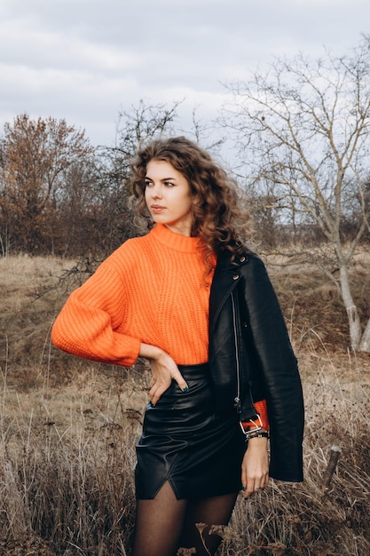 Foto junges lockiges mädchen in einem orangefarbenen pullover vor dem hintergrund der herbstnatur