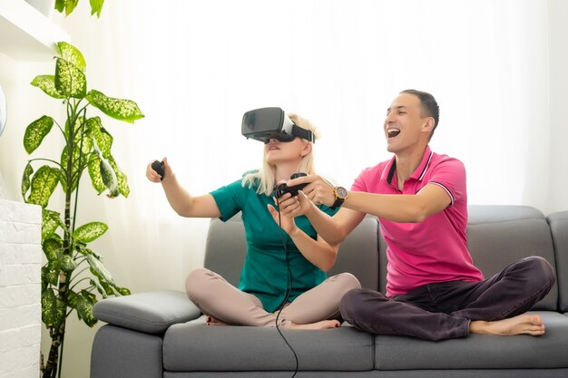 Junges lustiges Paar, das in ihrer Wohnung eine Virtual-Reality-Brille spielt - Glückliche Leute, die Spaß mit der neuen Trendtechnologie haben - Gaming-Konzept - Fokus auf Frauen-Joypad