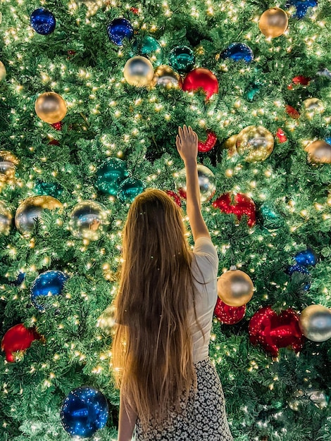 Junges Mädchen auf dem Hintergrund des Weihnachtsbaums in Miami Schöner Weihnachtsbaum in der beliebten Gegend am Weihnachtsabend und Lichter