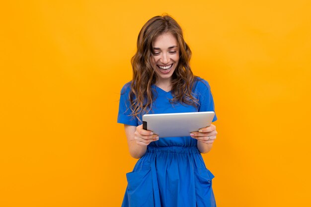 Junges Mädchen auf einer orange Oberfläche mit einer Tablette in ihren Händen