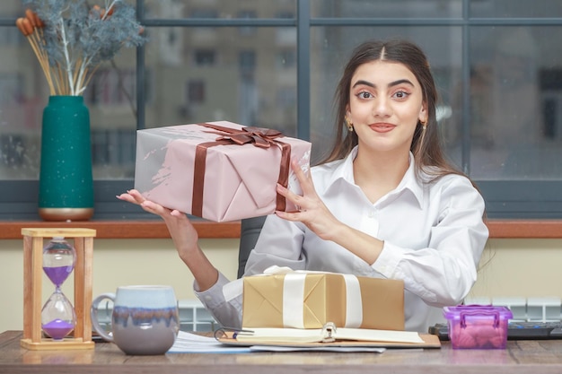 Junges Mädchen, das am Schreibtisch sitzt und eingewickelte Geschenkbox hält