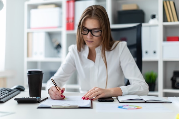 Junges Mädchen, das am Tisch sitzt und mit einem Computer, Dokumenten und einem Taschenrechner arbeitet