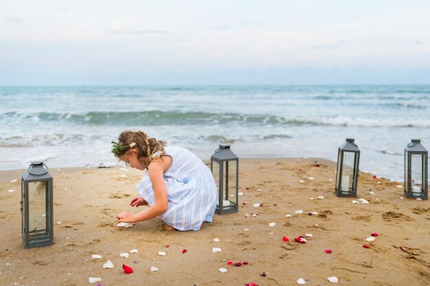 Foto junges mädchen, das blumenblumenblätter am strand sammelt