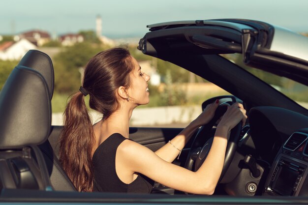 Junges Mädchen, das Cabrioauto, auf Sonnenunterganglicht fährt