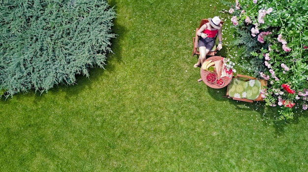 Junges Mädchen, das draußen im Sommergarten isst Frau hat ein Picknick und entspannt sich in der Luftaufnahme des Parks