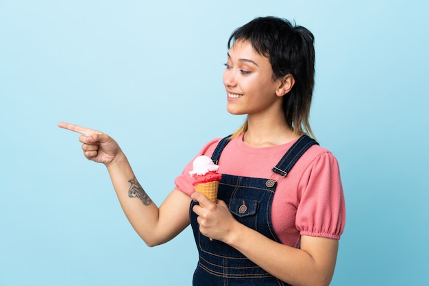 Junges Mädchen, das ein Kornetteis über der blauen Wand hält, die zur Seite zeigt, um ein Produkt zu präsentieren