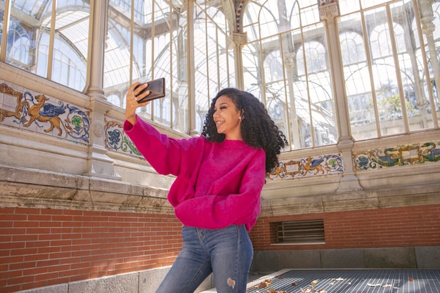 Junges Mädchen, das ein Selfie auf ihrem Handy macht, während sie auf ihren Freund wartet