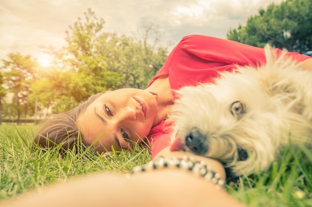 Junges Mädchen, das ein selfie mit ihrem Hund nimmt, der auf dem Gras am Park liegt
