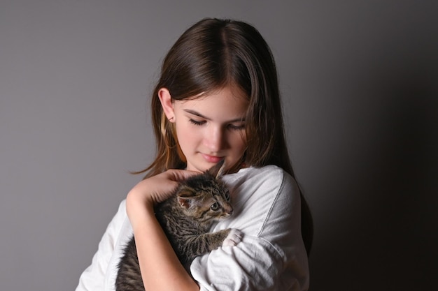 Junges Mädchen, das eine Babykatze auf grauem Hintergrund hält Weibchen, das ihr süßes Kätzchen umarmt Entzückendes Haustierkonzept