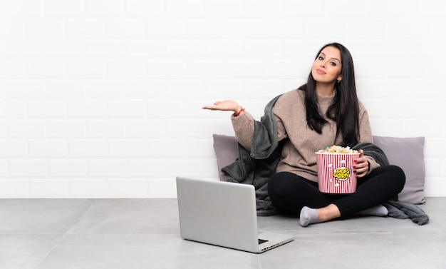 Junges Mädchen, das eine Schüssel Popcorn hält und einen Film in einem Laptop zeigt, der copyspace hält, um eine Anzeige einzufügen