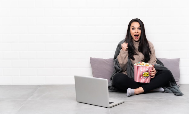 Junges Mädchen, das eine Schüssel Popcorn hält und einen Film in einem Laptop zeigt, der einen Sieg in der Siegerposition feiert