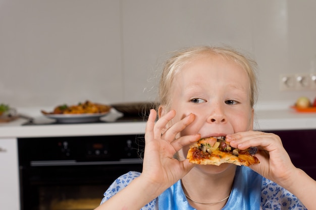 Junges Mädchen, das einen Bissen von hausgemachter italienischer Pizza nimmt und seitwärts blickt, während sie hungrig ihr Essen genießt