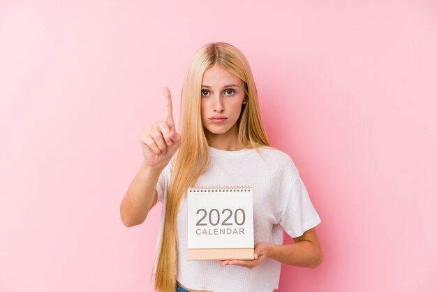 Junges Mädchen, das einen Kalender 2020 zeigt Nummer Eins mit dem Finger hält.