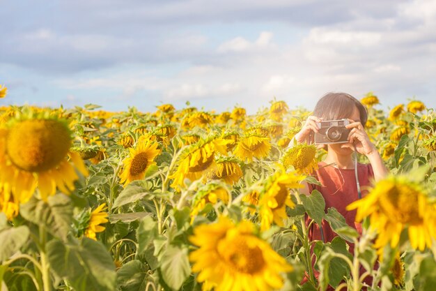 Junges Mädchen, das Filmkamera mit schönem Sonnenblumenfeldhintergrund hält