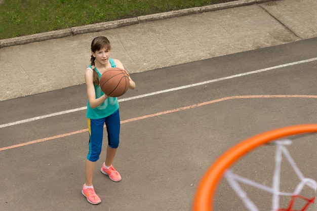 Junges Mädchen, das für die Basketballmannschaft übt, die das Ziel anvisiert, von oben auf dem Reifen gesehen?