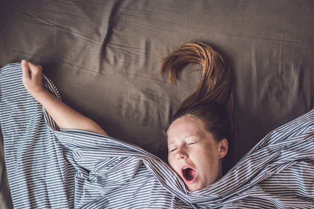 Junges Mädchen, das im Bett unter einer Decke liegt